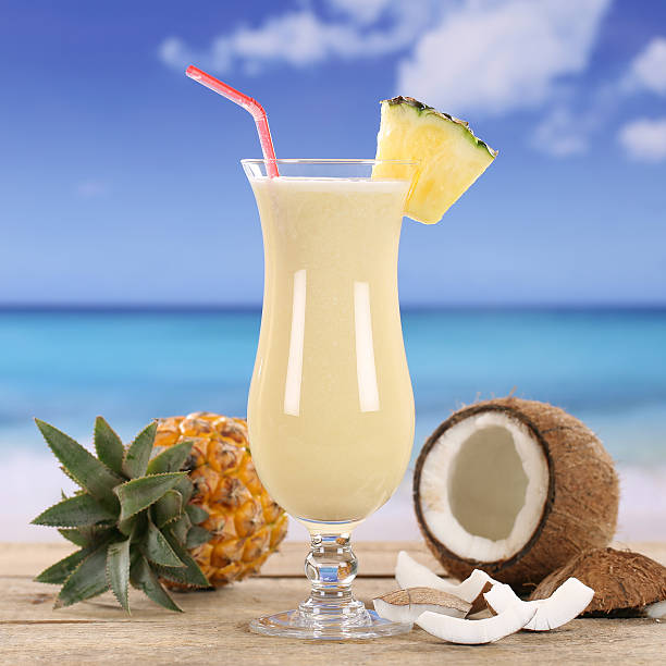 Piña colada in a tall glass with pineapple wedge on a table overlooking a tropical beach