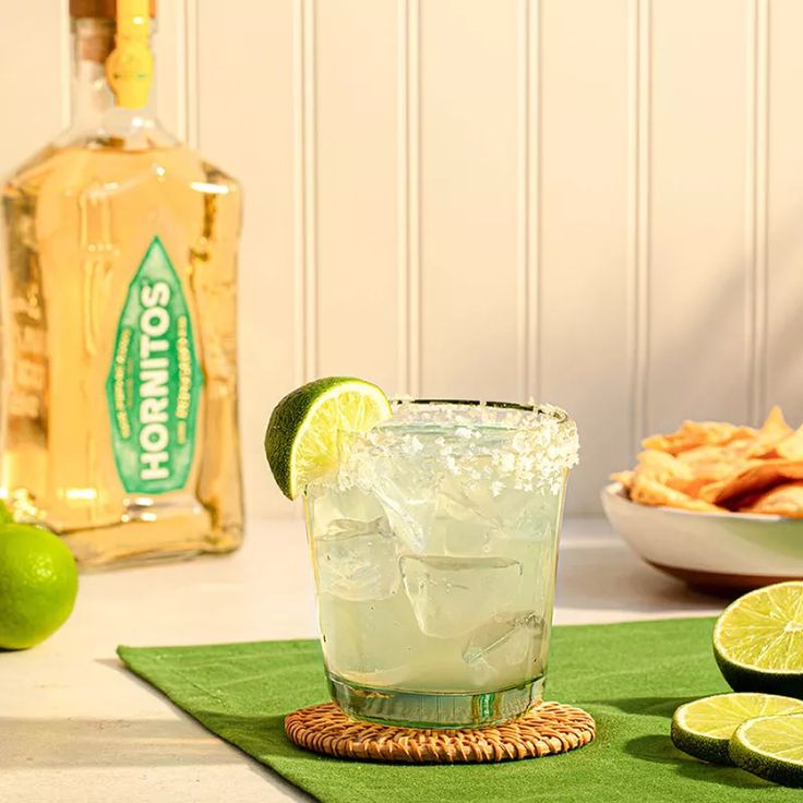 Margarita with a salted rim next to a bottle of blanco tequila and fresh agave leaves