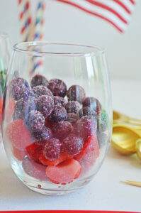 Layered frozen strawberry slices with frozen blueberries in a stemless wine glass.