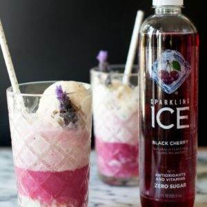 A bottle of Black Cherry Sparkling Ice next to two boozy black cherry floats on a marble table.