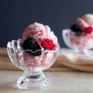 Boozy berry ice cream on a wooden table garnished with a blackberry and a red carnation.
