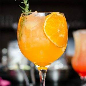 Orange Mango Mimosa on a bar garnished with an orange slice and rosemary sprig.