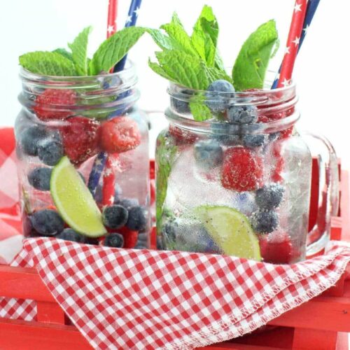 Two raspberry and blueberry silver tequila mojitos sitting on a red gingham napkin in a red tray with patriotic drinking straws.