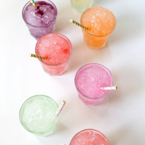 7 Sparkling Slush beverages on a white table with rainbow striped straws.