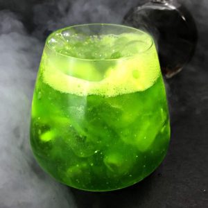A green, bubbling cocktail surrounded by smoke on a black backdrop.