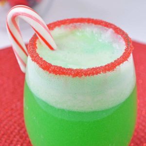 A green fizzy sherbet punch in a red sprinkle coated glass with a candy cane.