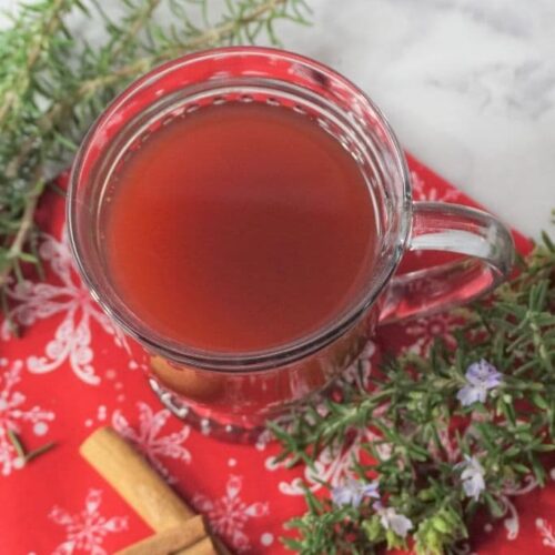 A glass of red mulled wine on a snowflake tablecloth with rosemary.