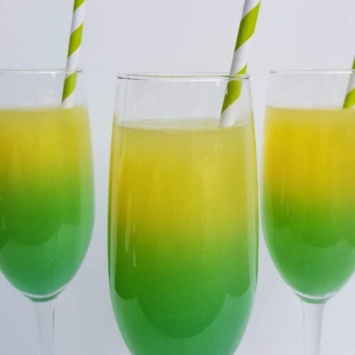 Pot of Gold Mimosas Recipe made with champagne, blue curacao, orange juice and vodka. The yellow and green cocktail is served in a champagne flute with a paper straw.