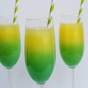 Recipe for Pot of Gold Mimosas served in a champagne flute with a green and white striped straw. Made with champagne, orange juice, vodka and blue curacao.