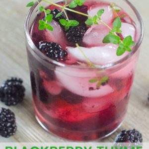 Cocktail made with fresh blackberries served in a glass, garnished with a sprig of fresh thyme.