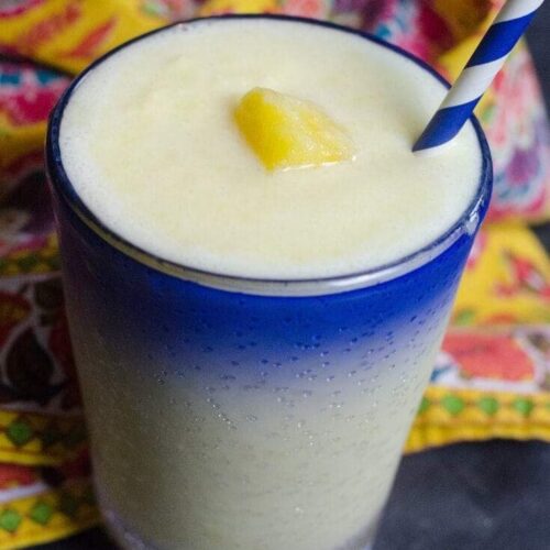 Pineapple Dole Whip Margarita served in a clear glass with a blue rim on a slate background with colorful napkin.