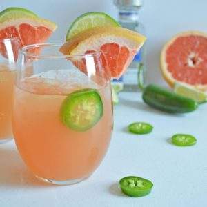 Two grapefruit and jalapeno margaritas with sliced fruit and a bottle of tequila