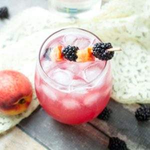 Blackberry Peach Drink on a wood table with fresh peaches and blackberries and a lace napkin