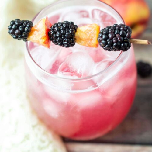 Vodka cocktail garnished with blackberries and peaches on a skewer