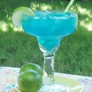An electric blue margarita on a pastel table cloth with two limes