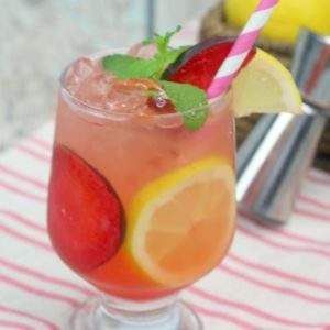 A cocktail with plums garnished with a pink striped straw.