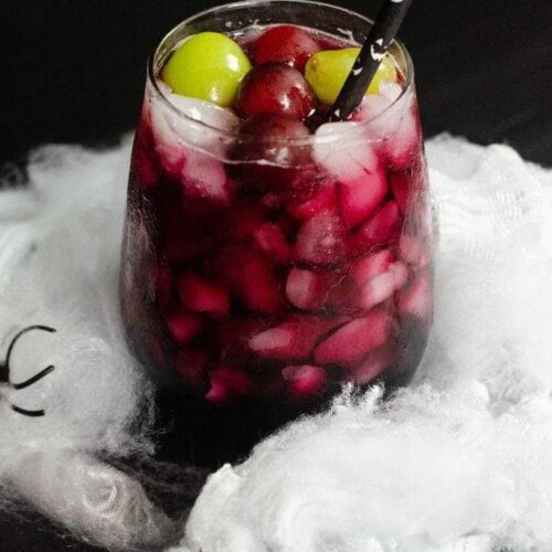 Cocktail with grapes and a Halloween straw surrounded by fake spiderwebs and spiders