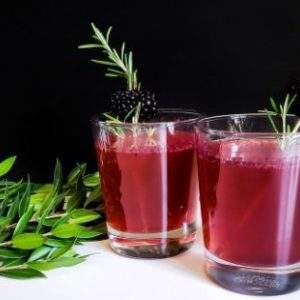 Two blackberry fireball whiskey fizz cocktails on a white table garnished with fresh rosemary and blackberries.