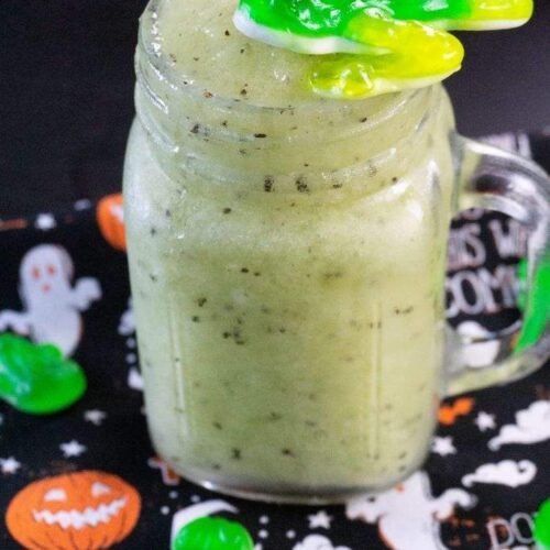 Kiwi slushie with frog gummy garnish served in a mason jar with a Halloween napkin.