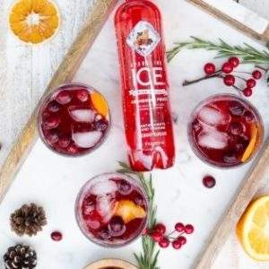 A serving tray holding 3 cranberry cocktails, a bottle of Sparkling Ice, pine cones, and orange slices.