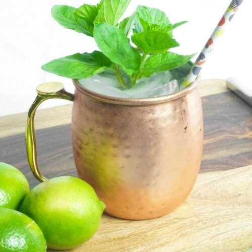 A copper mule mug garnished with mint next to some limes.