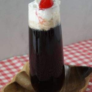 A cocktail in a stemless champagne glass topped with whipped cream and a cherry.