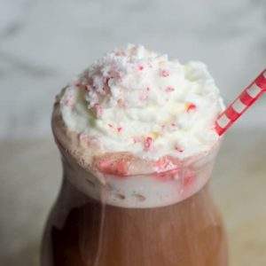 A small hurricane glass filled with peppermint hot chocolate topped with whipped cream and crushed peppermint and a straw.