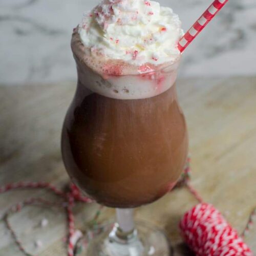 A hurricane filled with peppermint hot chocolate topped with crushed peppermint and whipped cream with red and white festive string.