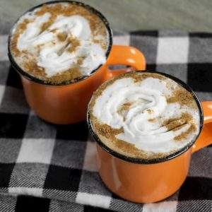 Orange mugs on buffalo plaid napkins filled with espresso topped with whipped cream and cinnamon