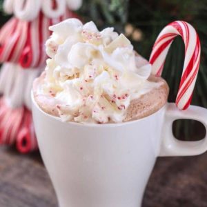 A white mug overflowing white hot chocolate, whipped cream, and a candy cane.