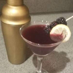 A blackberrymartini garnished with fresh blackberries and lemon with a gold cocktail shaker.