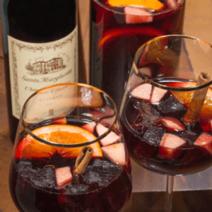 Two wine glasses filled with holiday red sangria with a bottle of chianti.