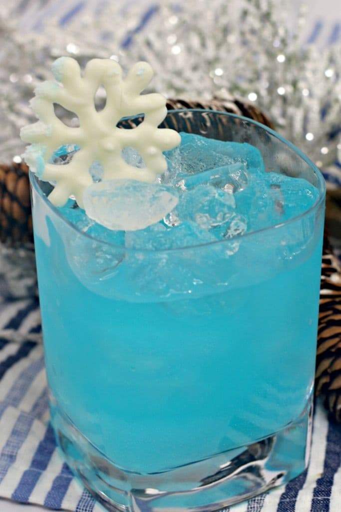 An electric long island iced tea, Elsa's Frozen cocktail, garnished with a snowflake on a striped napkin.