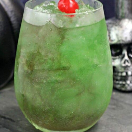 A shimmery green cocktail inspired by Harry Potter, the Death Eater's draught sits next to a silver skull.
