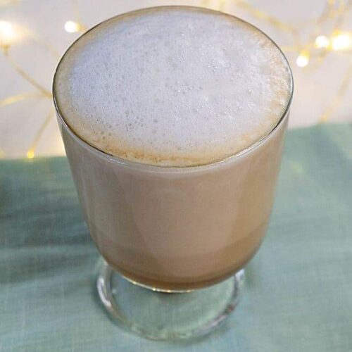 A London Fog Latte in a glass mug on a blue napkin in front of twinkle lights.