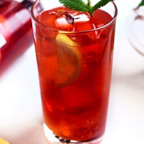 A highball glass filled with pomegranate lemonade next to a bottle of vodka lying on its side.