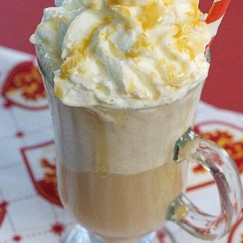 A tall clear mug filled with a butterbeer float topped with whipped cream on a Gryffindor placemat.