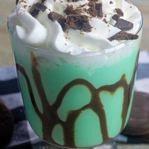 A glass filled with a chocolate mint cocktail topped with wipped cream and chocolate cookie pieces.