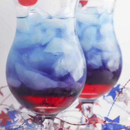 Two glasses of red and blue layered patriotic punch garnished with a cherry.