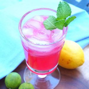 A bright pink cocktail on a blue napkin and wood platter garnished with mint.