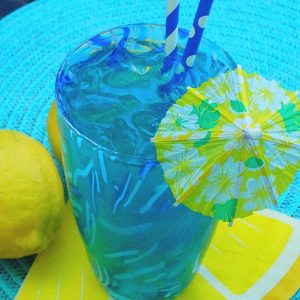 A yellow umbrella and blue paper straws sit in a blue drink.