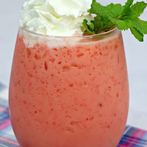 A frozen pink drink topped with whipped cream and fresh mint on a plaid napkin.