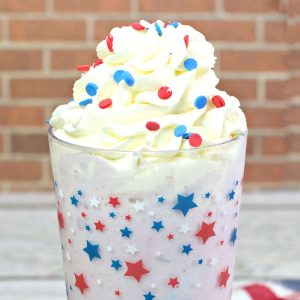 A milkshake in a glass with stars on it topped with whipped cream and sprinkles.