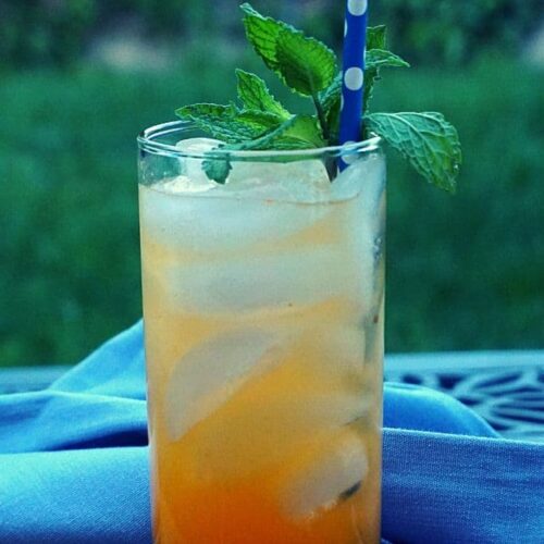 An orange beverage garnished with mint with a blue towel on an outdoor table.