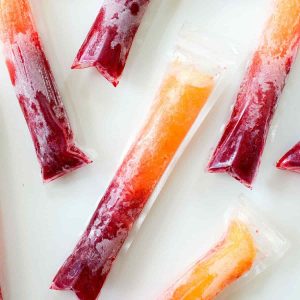 Raspberry peach popsicles in disposable popsicles tubes on a white table.