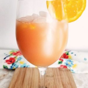 A close up of a wine glass filled with punch, garnished with an orange slice on a wood board.