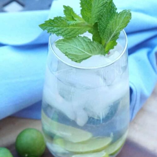 A cucumber and lime cocktail garnished with fresh mint on a platter with a wood napkin.