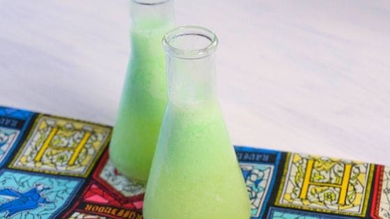 Two beakers of a green potion on a white table with a Hogwarts napkin.