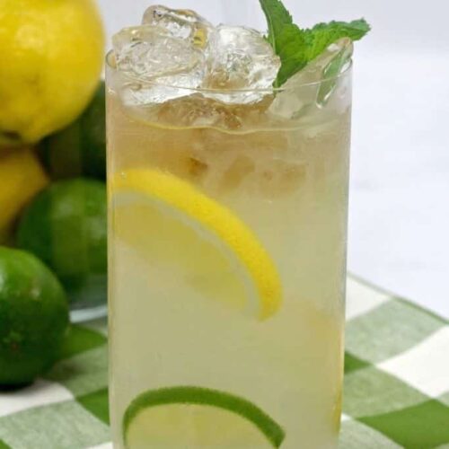 A highball glass filled with lemonade garnished with fresh mint on a green and white napkin.