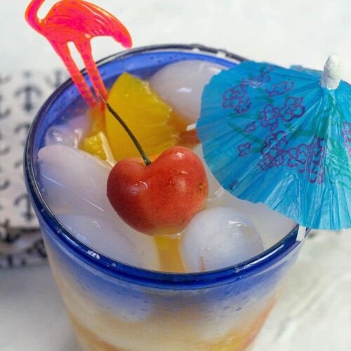 A cocktail garnished with a Rainier cherry, a blue umbrella and a pink flamingo pick.